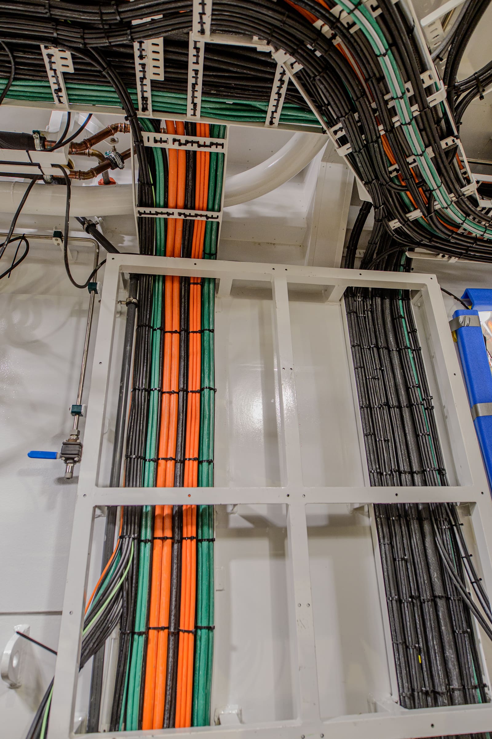 Vertical cable run with bundled orange, green and grey marine cables descending through a guarded support frame