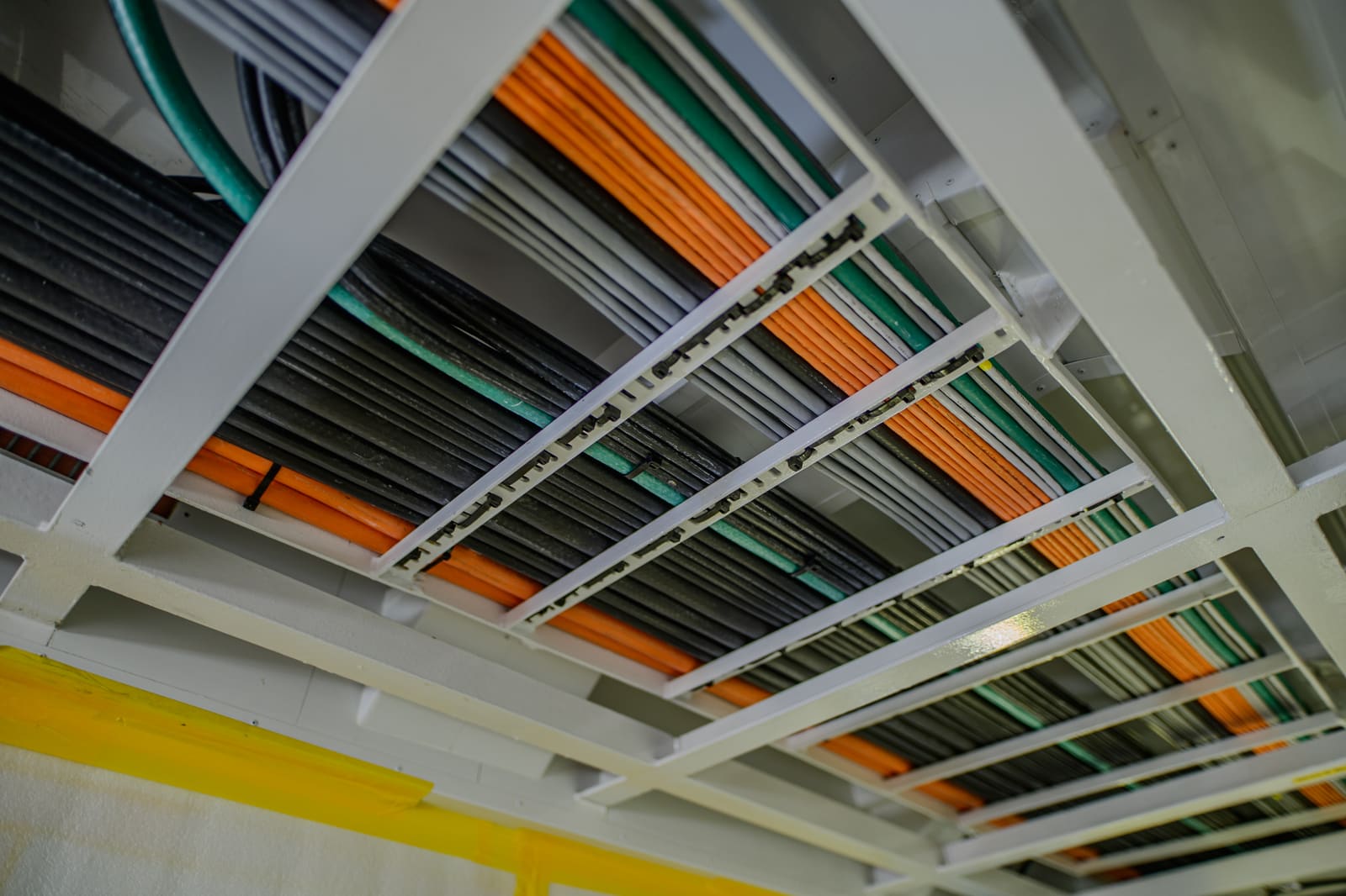 Cable trays packed with orange and green low-voltage marine cables along an engine room overhead