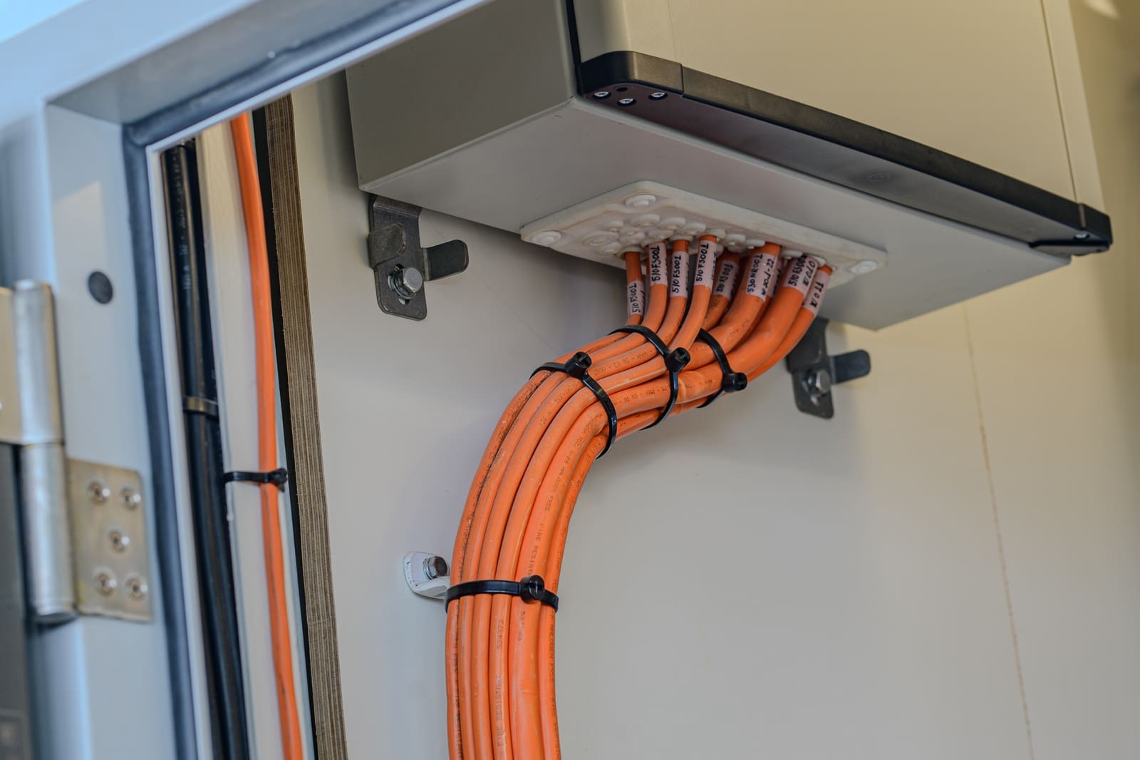 Cabinet bottom entry with bundled orange marine signal cables sweeping into the enclosure through a sealed cable gland plate
