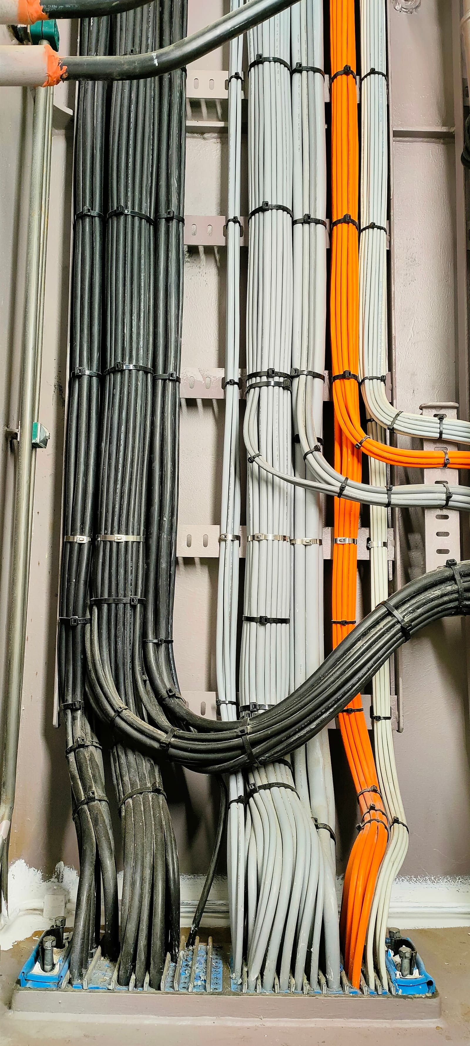 Vertical cable highway with grey, black and orange marine cables routed in parallel along bulkhead-mounted ladder supports