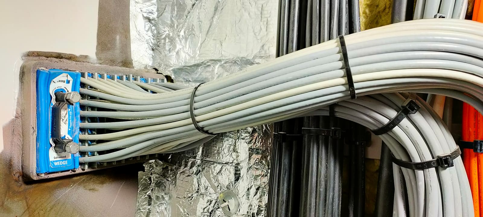 Wide bundle of marine cables exiting a multi-cable transit block on an insulated bulkhead, secured with cable ties at regular spacing
