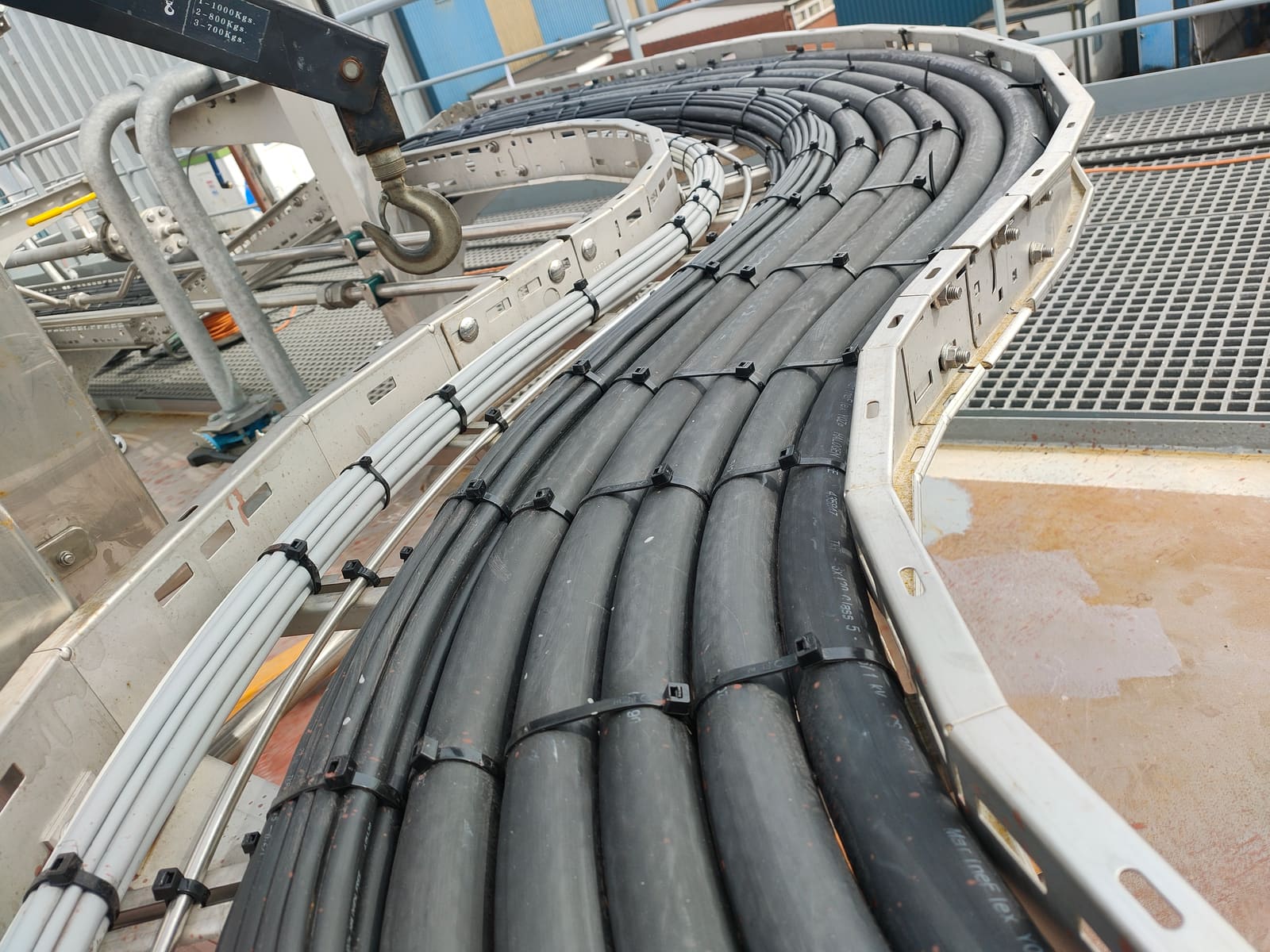Externally routed marine power cables on a curved cable tray running along a deck edge above sea-facing grating