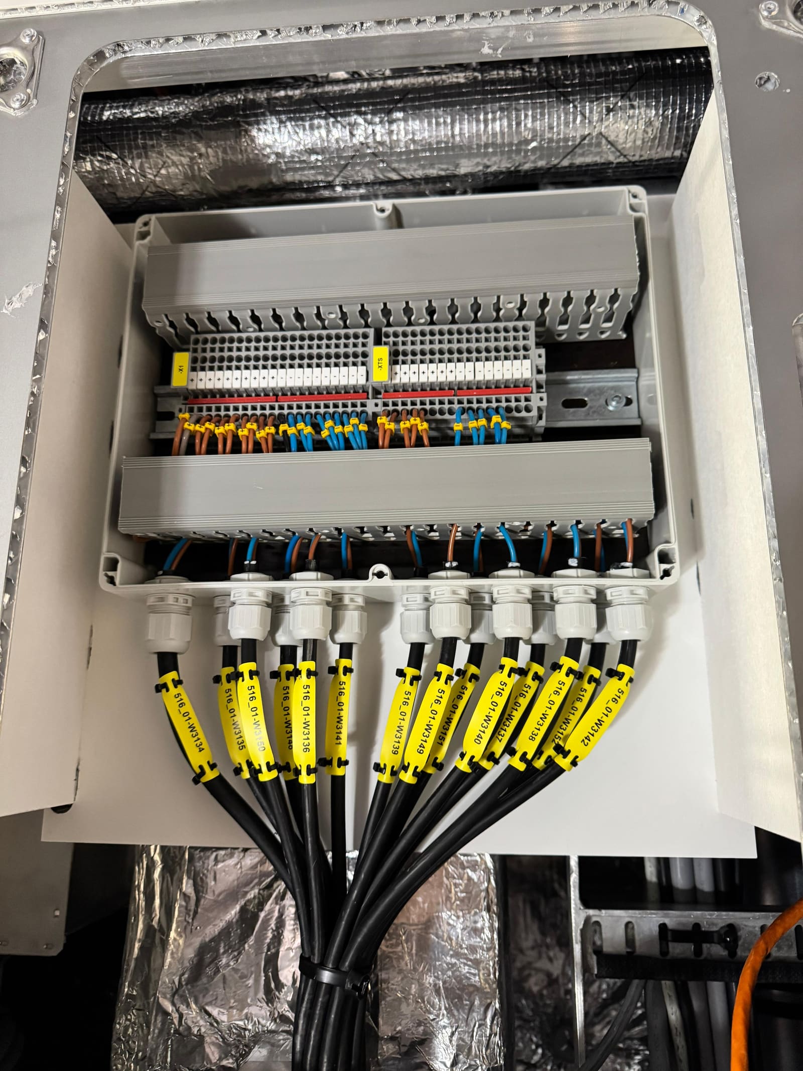Open IP-rated junction box with marine cables terminated to DIN-rail terminal blocks and labelled cable tags hanging below