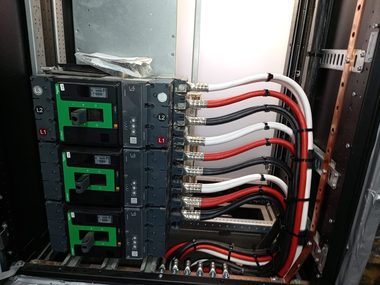Three-pole moulded-case circuit breakers in a marine switchboard with red, white and black power cables terminated to the line side