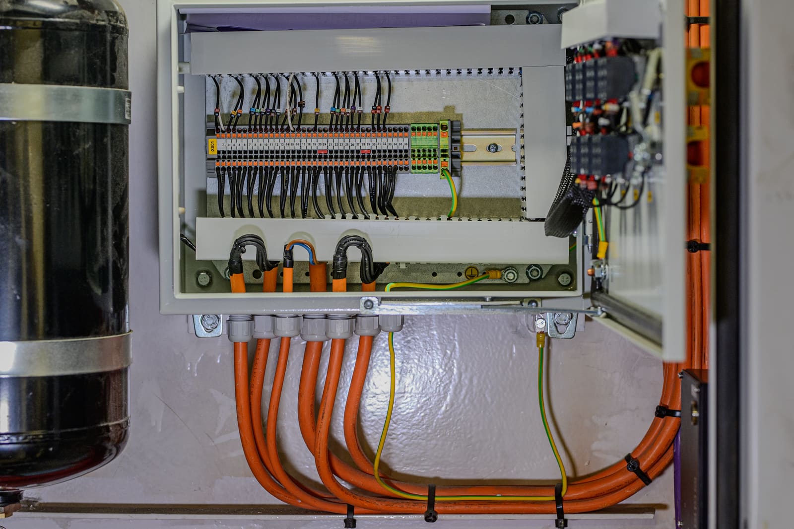 Junction box on bulkhead with terminated control cables on a DIN rail and orange marine cables routed in below through cable glands