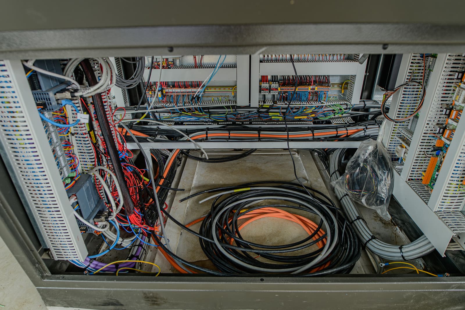 Inside view of a control cabinet bottom with grey, orange, and black marine cables routed onto a cable tray ready for termination