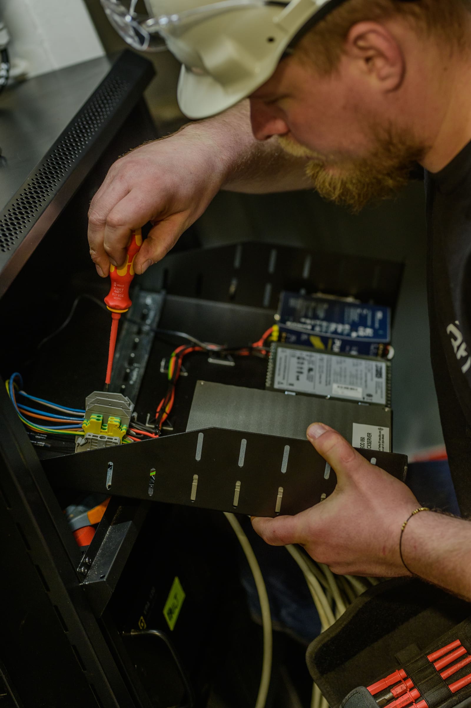 Black Frog Elektro technician in white hardhat terminating signal cables on a spring-clamp connector with insulated screwdriver