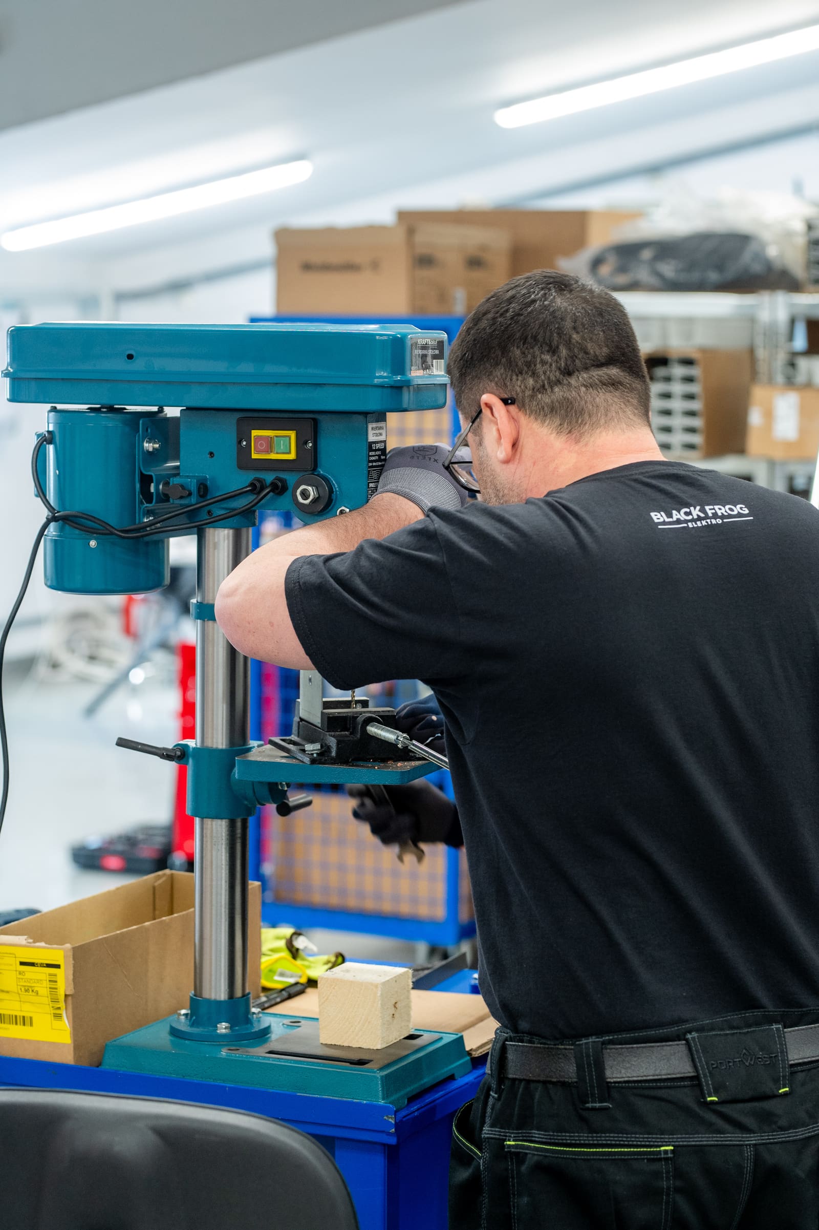 Black Frog Elektro panel builder drilling a mounting hole on a column drill press in the panel-building workshop
