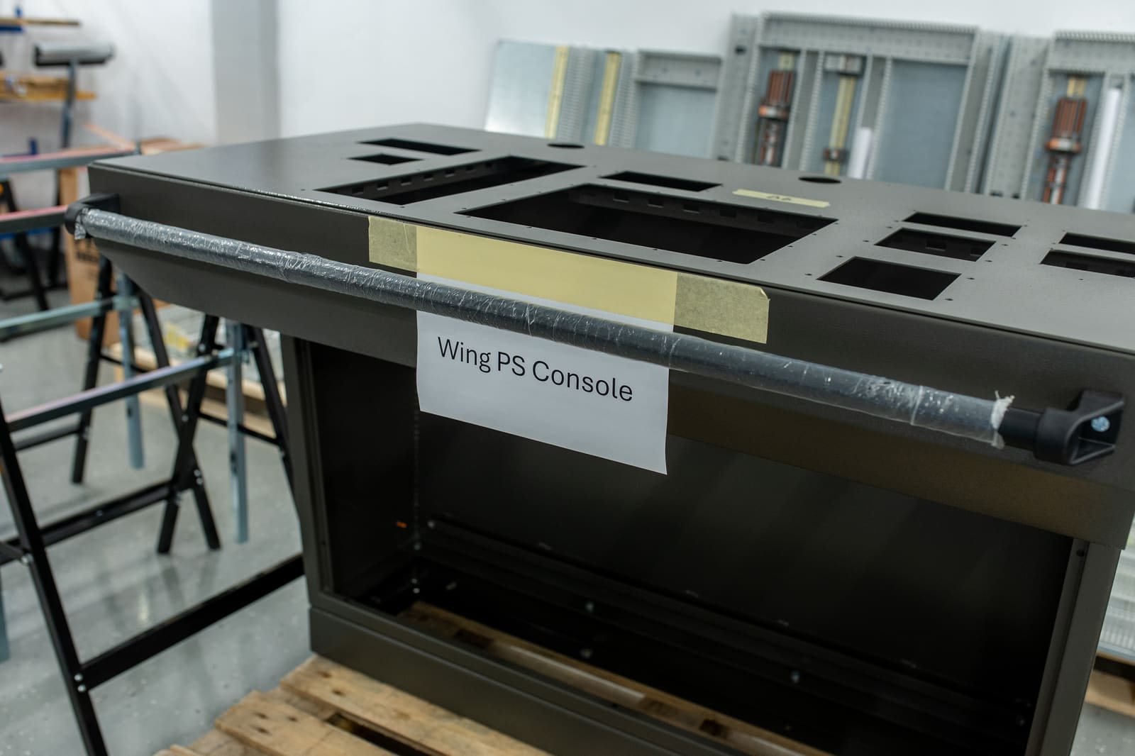 "Wing PS Console" labelled steel enclosure on trestles in the panel-building workshop, awaiting equipment fit-out