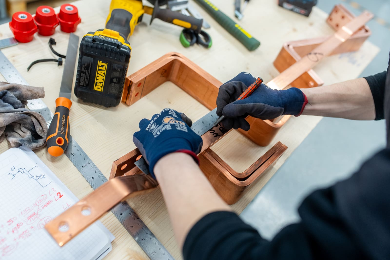 Close-up of a panel builder marking a freshly bent copper busbar with a measuring square on the workshop bench