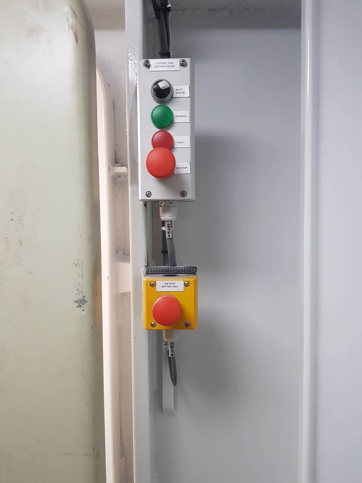 Pendant control stations with green start and red stop pushbuttons and a separate yellow emergency-stop enclosure mounted overhead