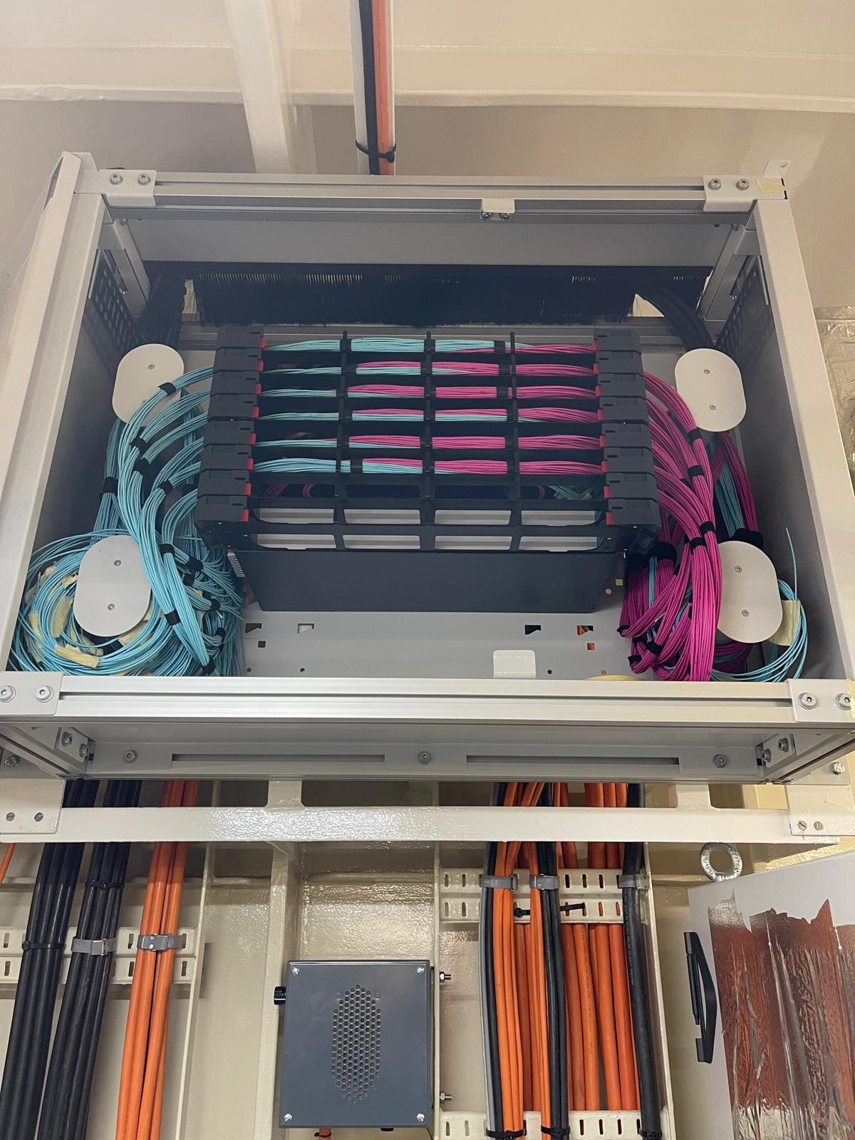 Marine fiber optic distribution cabinet with magenta and aqua patch cords organised onto splitter shelves above marshalling cabinet I/O